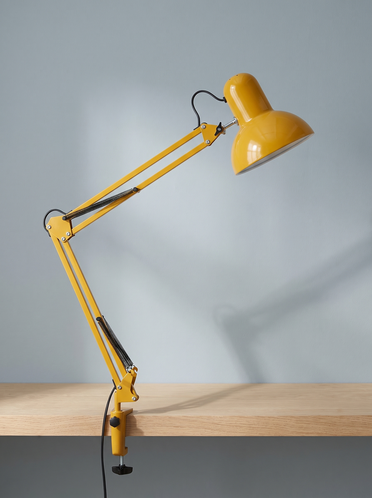 Otis architect clamp lamp in yellow on a dusty blue backdrop