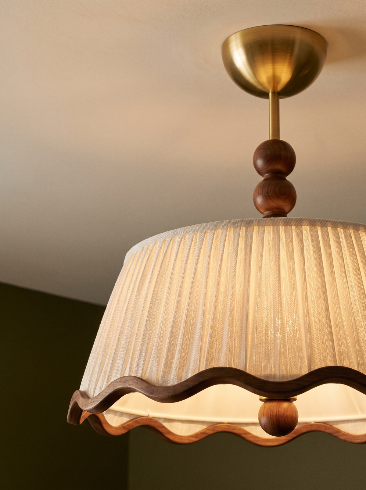 Lifestyle: close-up of Odette's pleated shade, wavy walnut trim and wood beads, lit