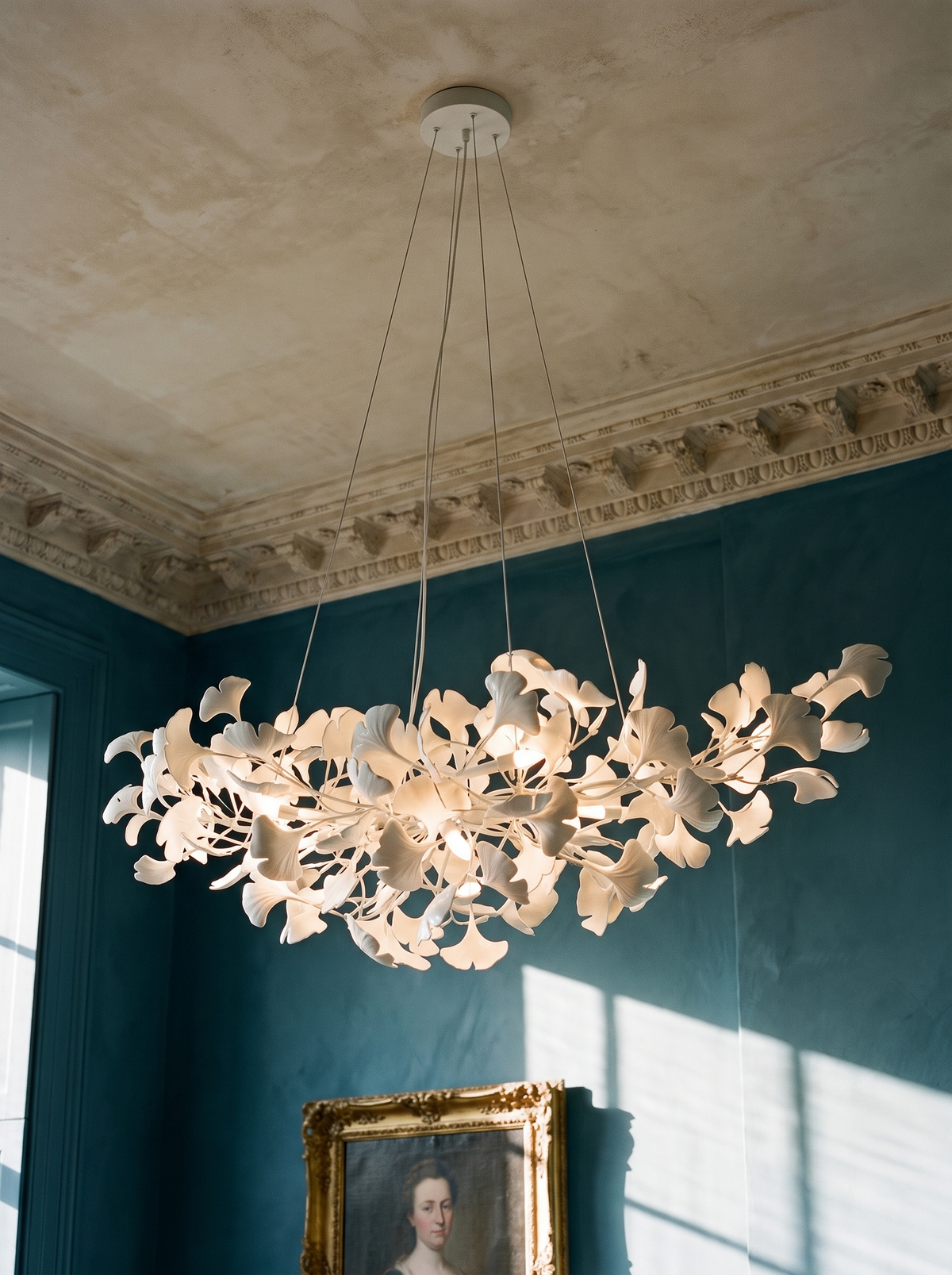 Ginevra porcelain ginkgo leaf chandelier in white against teal plaster