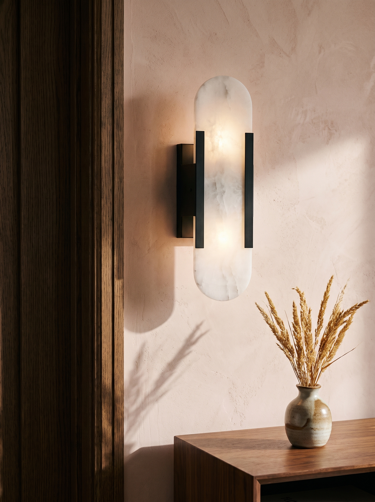 Romy alabaster wall sconce in black on a blush plaster wall
