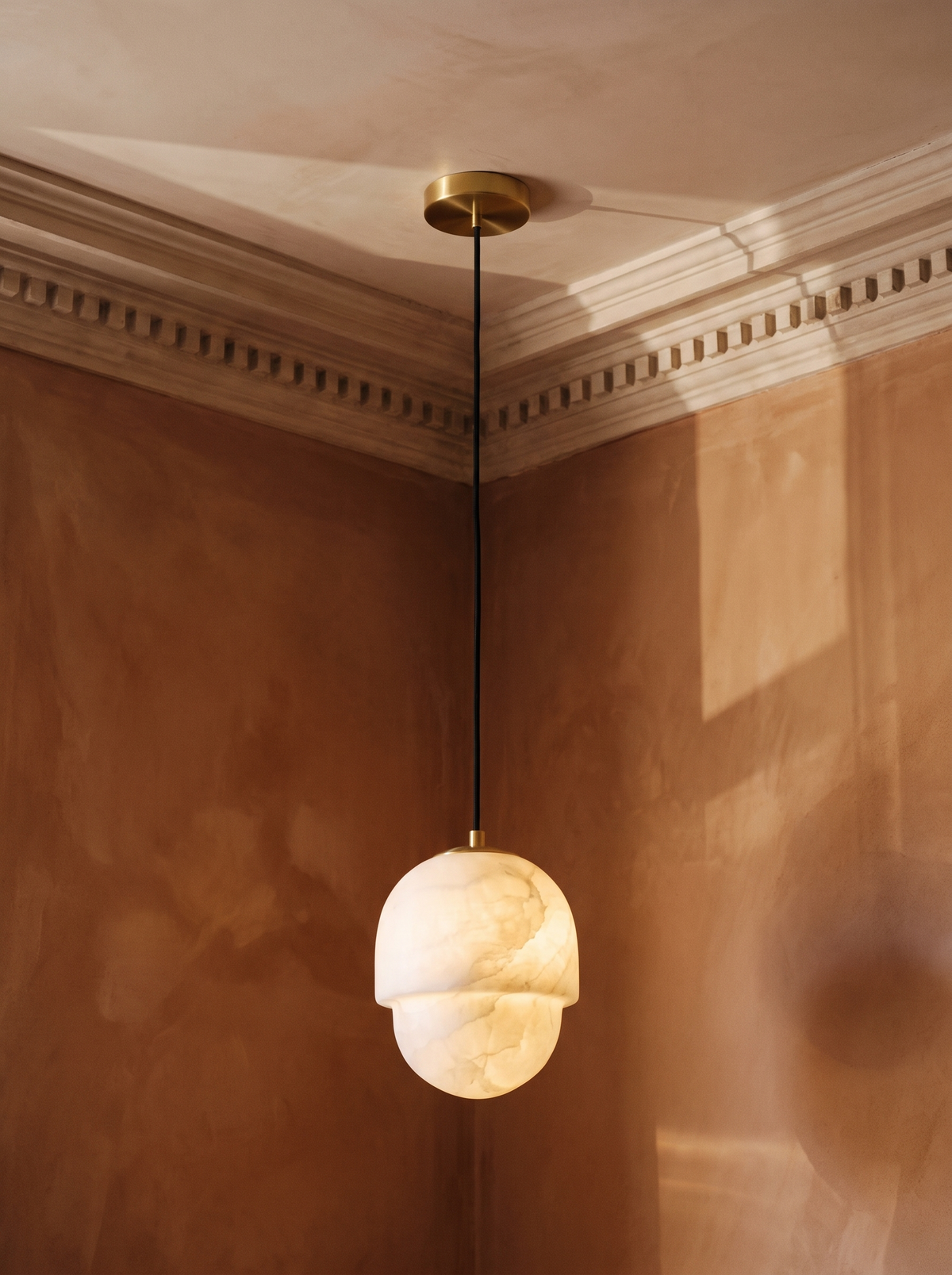 Oaklee acorn alabaster pendant light in brass hanging in a sienna plaster-moulded corner