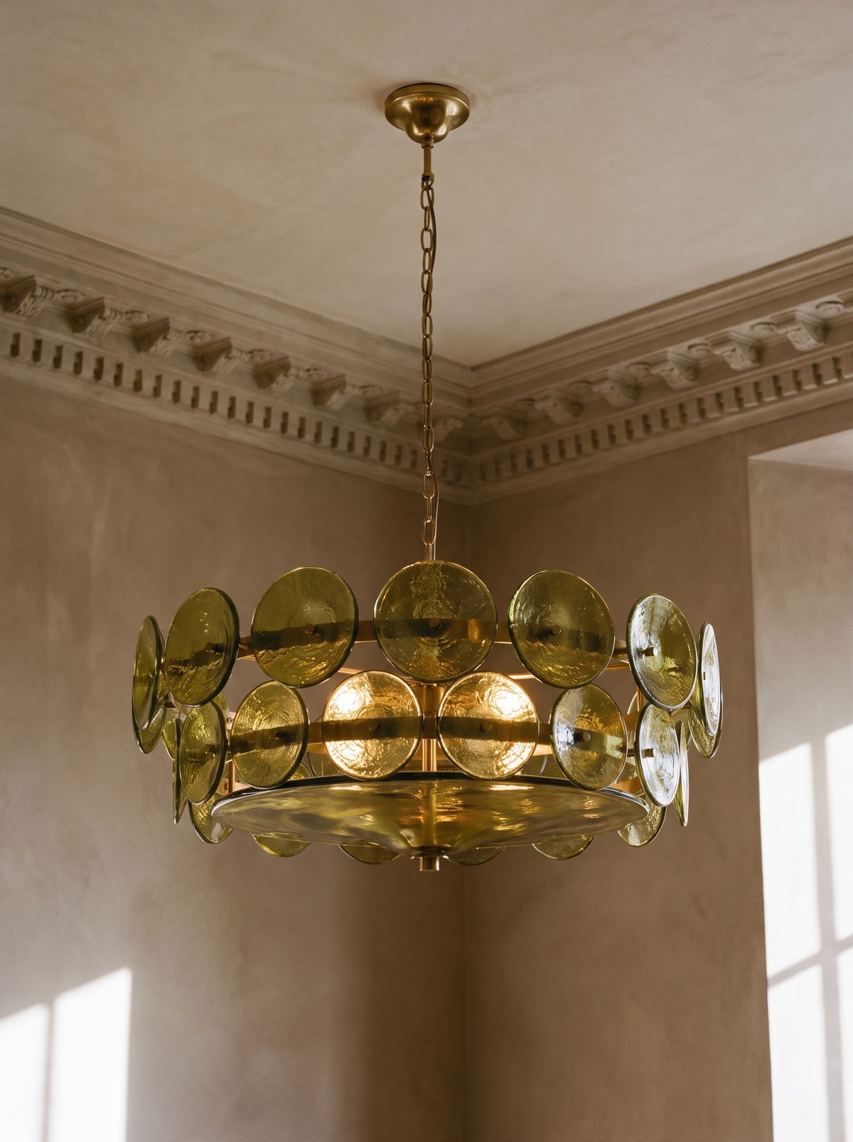 Soleil olive-green glass disc chandelier hanging in a plaster-moulded corner