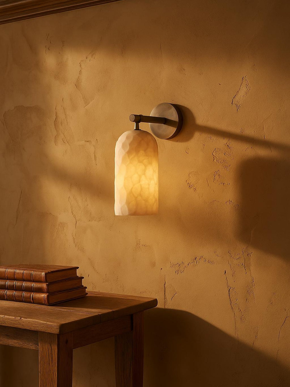 Pilar hand-faceted alabaster wall sconce in antique bronze on a clay-ochre plaster wall