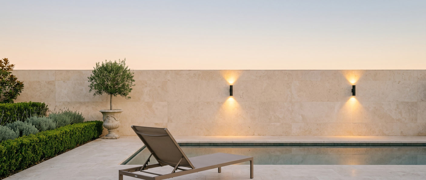 A pair of Vega wall lights on a travertine pool wall at dusk, lifestyle scene