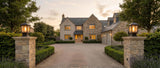 A pair of Gable lanterns on stone gate pillars at a driveway entrance at dusk, lifestyle scene