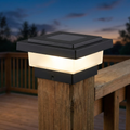 Black solar post cap light glowing warm white on a wooden fence post at dusk