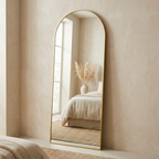 Gold framed arched full-length floor mirror leaning against a bedroom wall