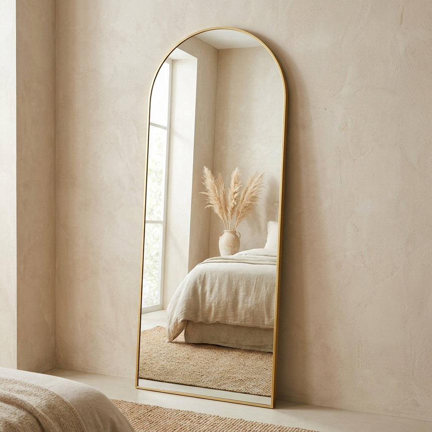 Gold framed arched full-length floor mirror leaning against a bedroom wall