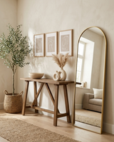 Selene arched gold mirror leaning in a full entryway with console, vases, bowl, art and olive tree — shop the whole collection