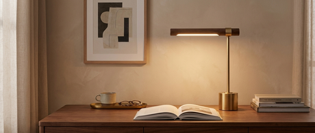 Ivo walnut-and-brass desk lamp glowing over a book on a walnut desk — lifestyle