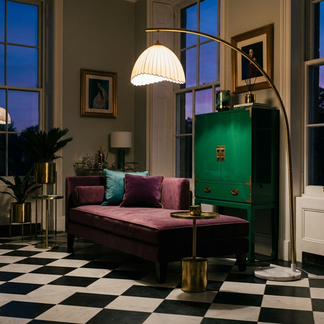 Arcadia arc floor lamp over a plum chaise with emerald cabinet, brass accents and checkerboard floor at dusk