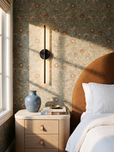 Lifestyle: black Tarn wall sconce on floral wallpaper beside a cognac headboard and travertine nightstand in a bedroom