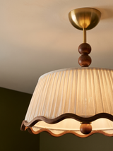 Lifestyle: close-up of Odette's pleated shade, wavy walnut trim and wood beads, lit