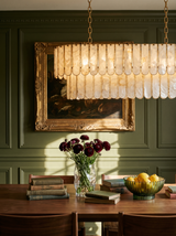 Lifestyle: Marelle oval shell chandelier glowing over a walnut dining table in an olive-panelled room