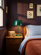 Lifestyle: green Bittel table lamp on an oak nightstand in a plum bedroom with botanical prints