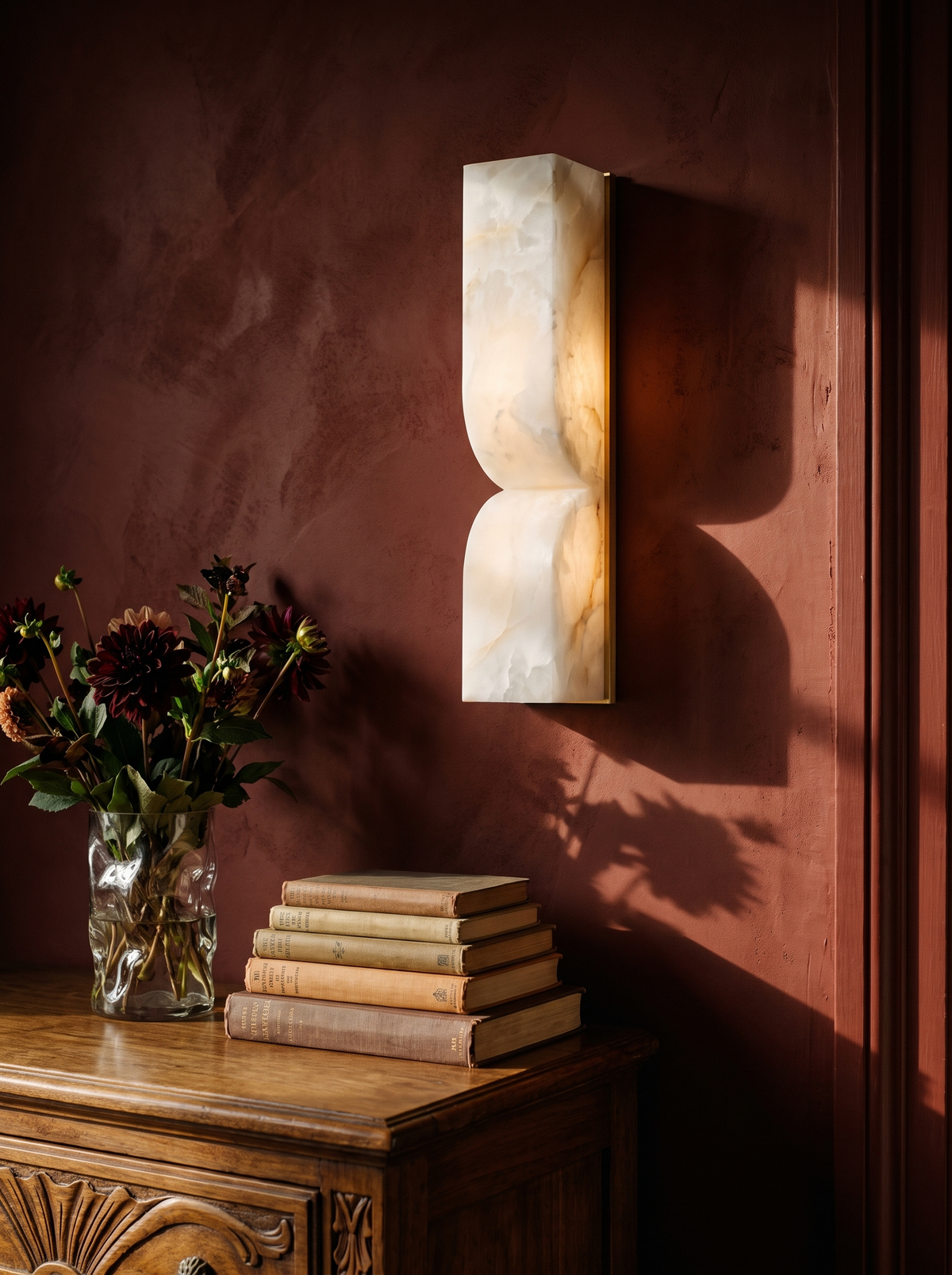 Aurelie carved alabaster wall sconce in gold and white on an oxblood plaster wall