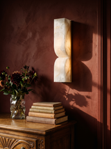 Aurelie carved alabaster wall sconce in gold and white on an oxblood plaster wall