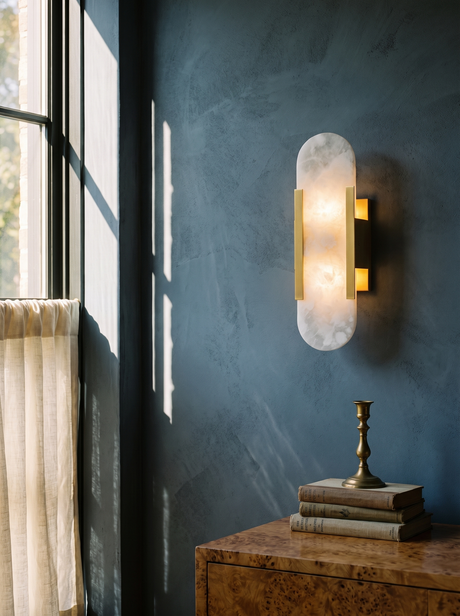 Romy alabaster wall sconce in brass on a slate-blue plaster wall