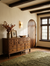 Lifestyle: Romy alabaster sconce above an oak apothecary cabinet in a beamed living room, showing its size