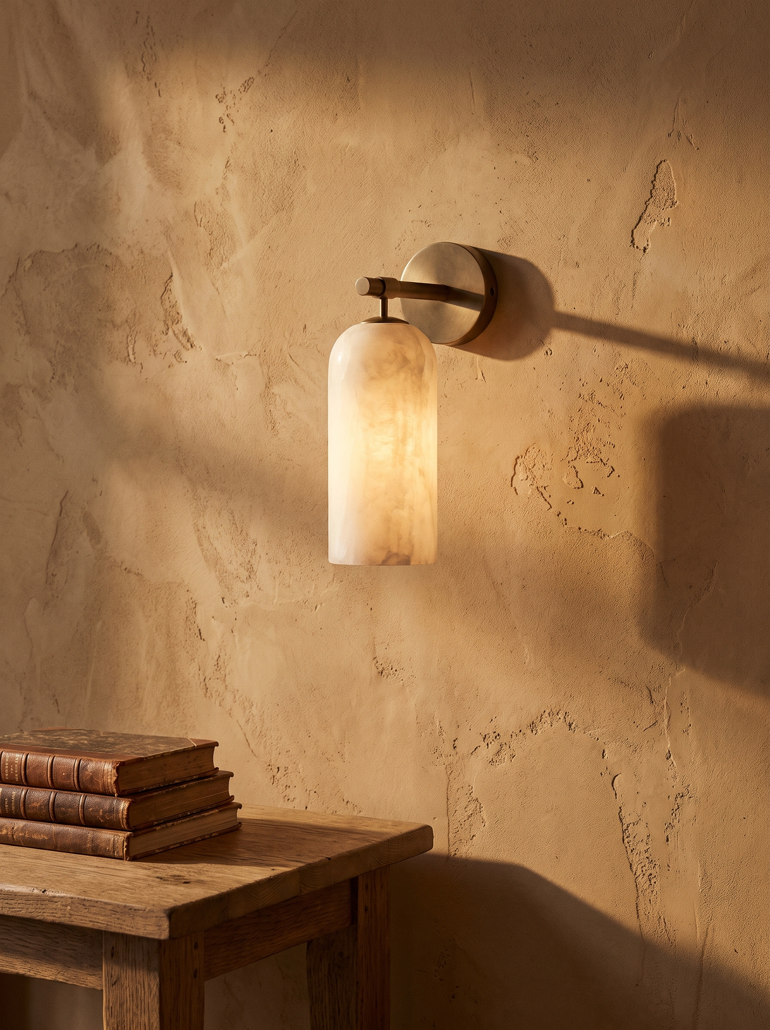 Pilar alabaster wall sconce in antique bronze on a clay-ochre plaster wall