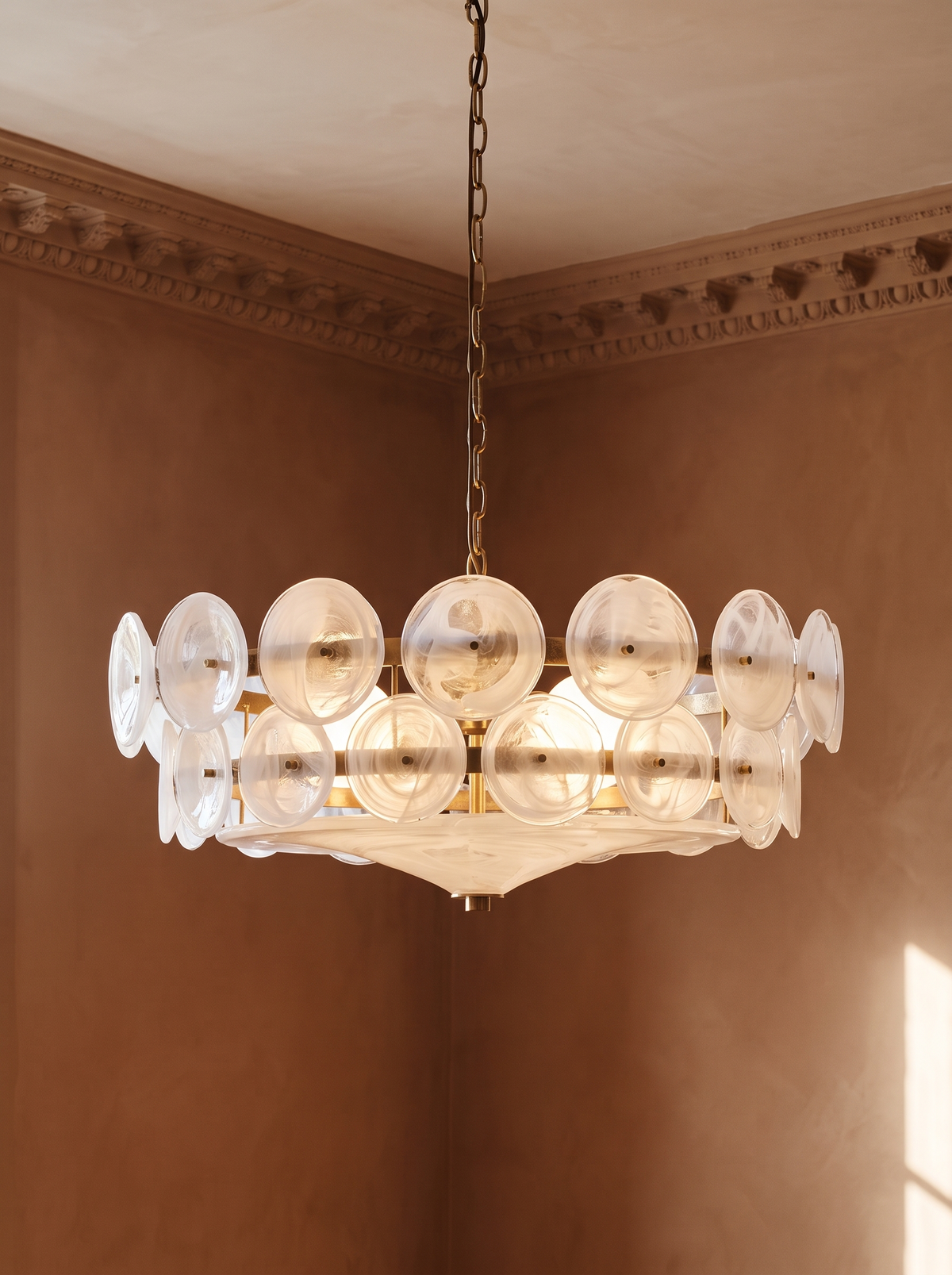 Soleil clear glass disc chandelier hanging in a plaster-moulded corner