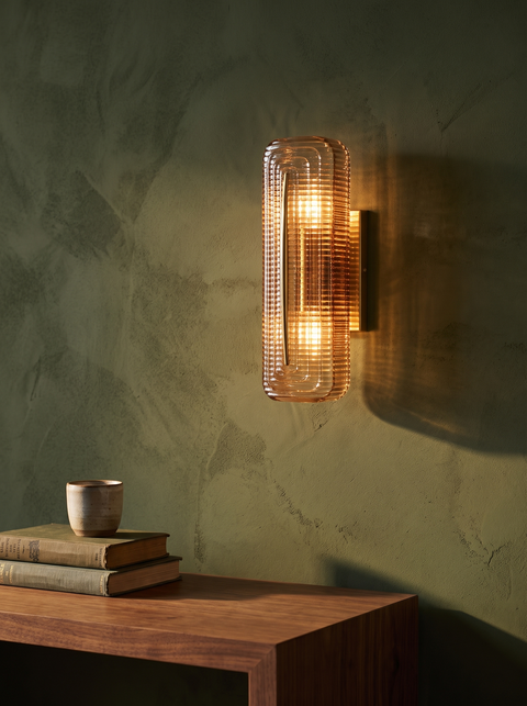 Calla fluted cognac glass wall sconce in brass on an olive-green plaster wall