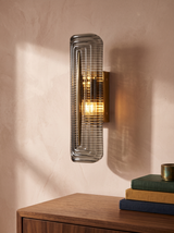 Calla fluted smoke-grey glass wall sconce in brass on a blush plaster wall