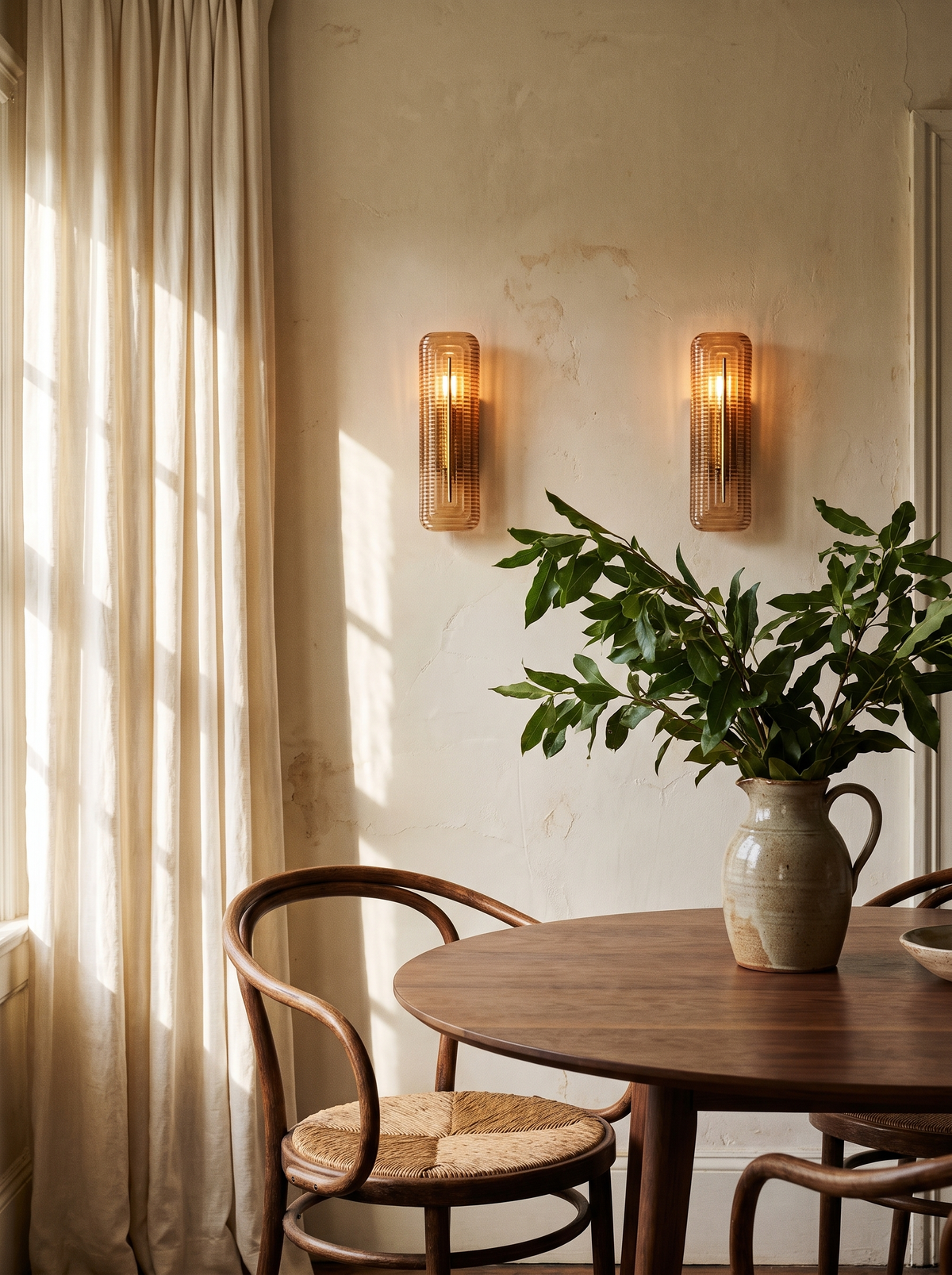 Lifestyle: a pair of Calla cognac glass sconces above a round walnut dining table