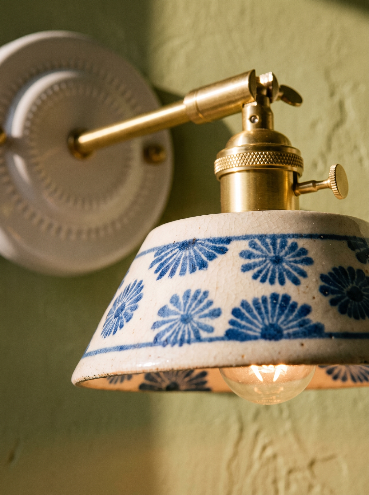 Lifestyle: close-up of Fable's hand-glazed blue daisy ceramic and brass arm, lit