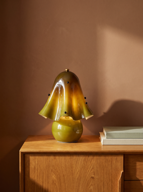 Petal green glass flower table lamp on an oak console against a warm plaster wall
