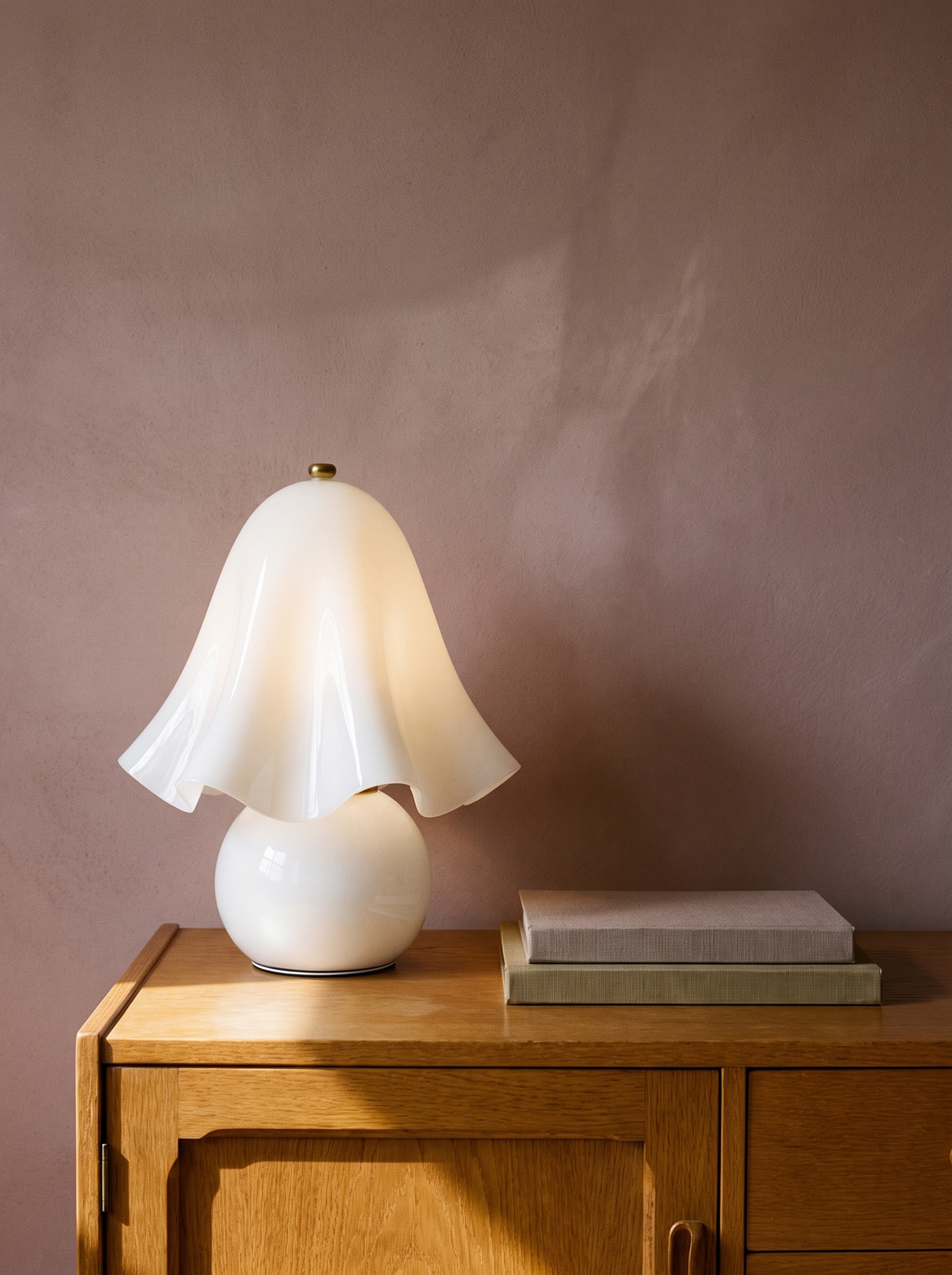 Petal white glass flower table lamp on an oak console against a warm plaster wall