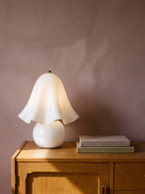 Petal white glass flower table lamp on an oak console against a warm plaster wall