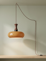 Toffee plug-in glass pendant light in caramel brown on a sage green backdrop