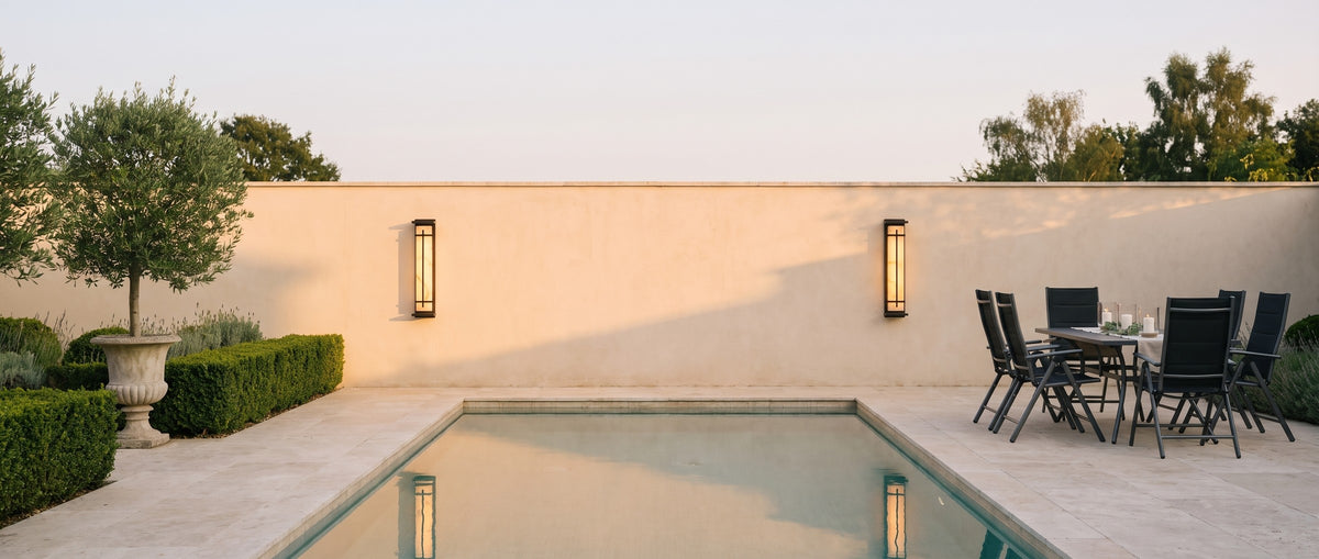 A pair of Luminara sconces on a travertine pool wall at dusk, lifestyle scene