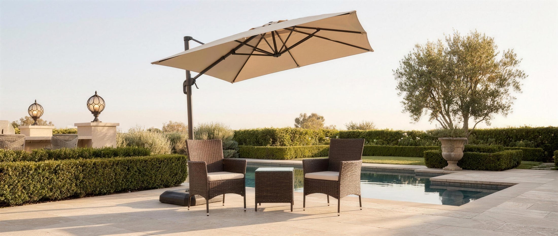 Sabbia wicker set under a beige umbrella on a poolside travertine terrace at golden hour — lifestyle