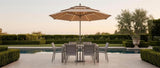 Sera umbrella with lit solar ribs over a poolside dining set at dusk — lifestyle