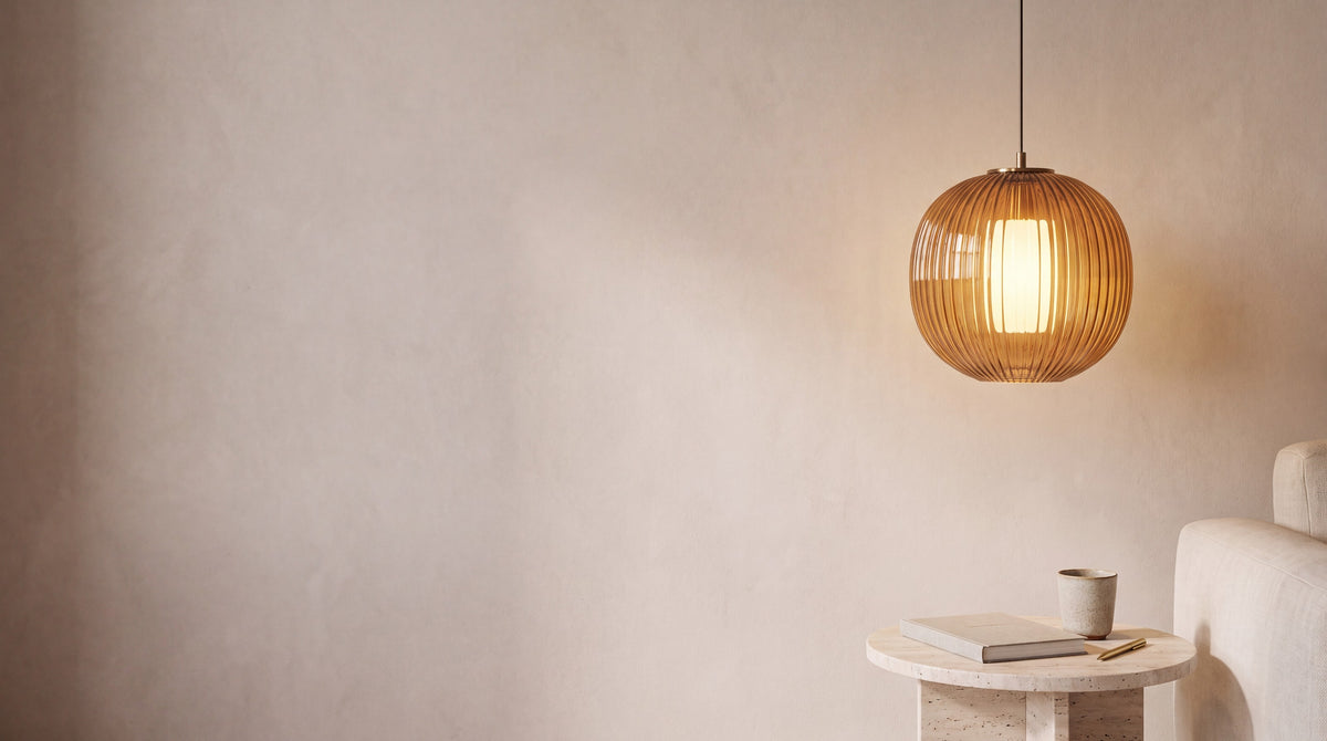 Amber ribbed glass pendant light above a travertine side table against a warm plaster wall
