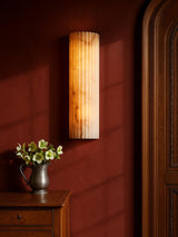 Clio medium ribbed alabaster wall sconce on an oxblood plaster wall