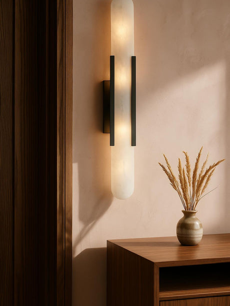 Romy tall alabaster wall sconce in black on a blush plaster wall