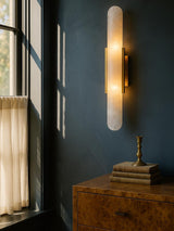 Romy tall alabaster wall sconce in brass on a slate-blue plaster wall