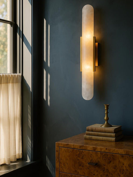 Romy tall alabaster wall sconce in brass on a slate-blue plaster wall