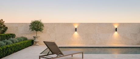 A pair of Vega wall lights on a travertine pool wall at dusk, lifestyle scene